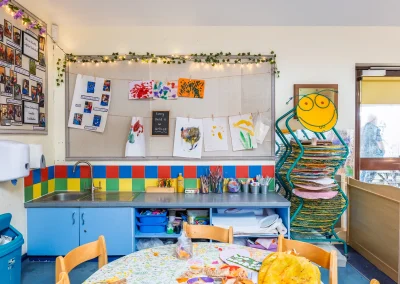Creative classroom area with children's paintings, art supplies and drying rack at Little Gems preschool