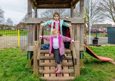 Children playing on a wooden outdoor climbing structure at Little Gems preschool