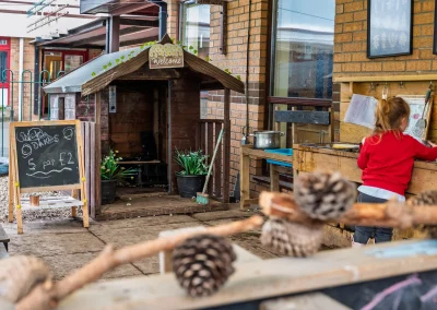 Child exploring the outdoor mud kitchen beside a wooden playhouse at Little Gems preschool