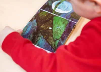 Child examining a colourful leaf picture during a classroom activity at Little Gems preschool