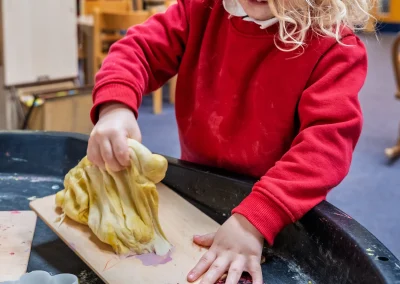 Child pressing and shaping yellow play dough at a creative activity table at Little Gems preschool
