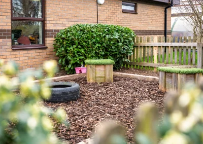 Outdoor sensory garden with bark, a tyre and grass-topped wooden blocks at Little Gems preschool